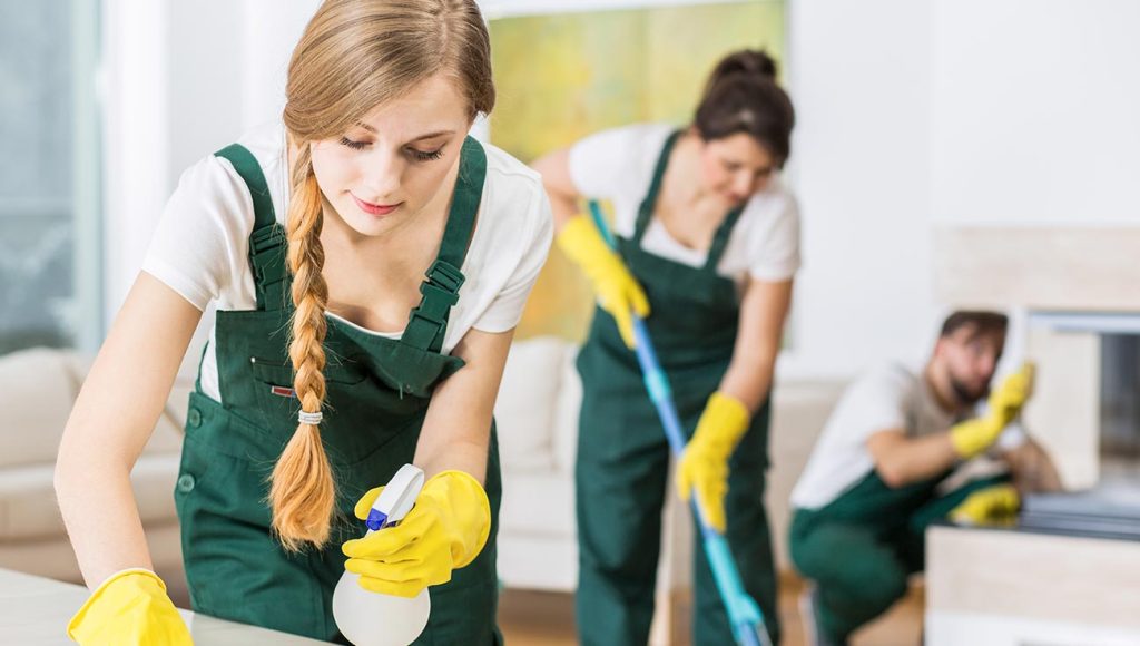 group of people cleaning room with yellow gloves and green aprons on